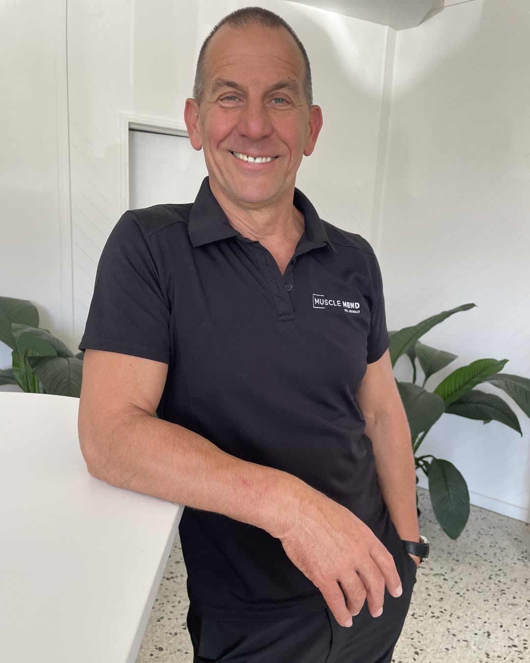 Mario leaning on the reception counter at Muscle Mend, smiling